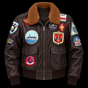 May include: A dark brown leather flight jacket featuring a brown faux fur collar, a front zipper, and ribbed cuffs. The jacket is decorated with numerous embroidered military-style patches, including text such as Texas, Dallas, Seabees, and USS William M. Standley.