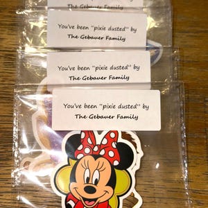 May include: A stack of clear plastic bags containing stickers, each with a white label printed with the text You've been "pixie dusted" by The Gebauer Family. The front sticker features a colorful illustration of Minnie Mouse.