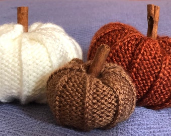 May include: Three knitted pumpkins, one white, one brown, and one orange, with cinnamon sticks for stems.