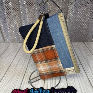 May include: A small patchwork denim and plaid zippered pouch with a cream-colored braided strap and a silver key ring.