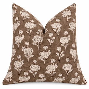 May include: A square throw cushion featuring a dark brown base colour with a repeating off-white floral pattern. The design displays multiple rose blossoms and buds with stems and leaves distributed evenly across the textured fabric surface.