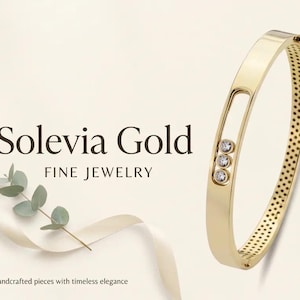 Puede incluir: Una pulsera rígida de oro con una abertura rectangular que contiene tres piedras redondas y transparentes engastadas. La pulsera tiene una superficie interior texturizada y perforada, y un cierre de bisagra. El texto Solevia Gold Fine Jewelry es visible.