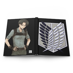 May include: An open hardcover book featuring a black cover. The left side displays an illustration of a character with dark hair wearing a light shirt and harness. The right side shows a white and dark blue shield emblem with wings and swords.