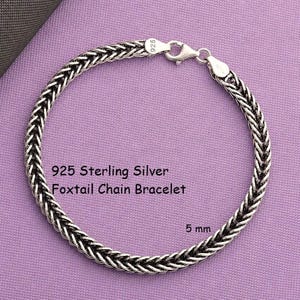 May include: A 925 sterling silver foxtail chain bracelet with a lobster claw clasp. The metal links feature a dark oxidised finish in the crevices. The text 925 Sterling Silver Foxtail Chain Bracelet and 5 mm are printed on the image.