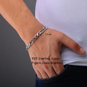 May include: A 925 sterling silver Figaro chain bracelet with a width of 7.5 mm. The bracelet features a classic interlocking link design with a polished metallic finish, clearly labeled as a 925 sterling silver Figaro chain bracelet.