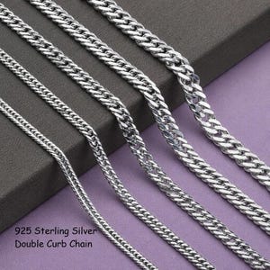 May include: Four silver-toned metal curb chains of varying thicknesses arranged diagonally. The chains feature interlocking flat links with a polished finish. The text 925 Sterling Silver Double Curb Chain is printed in the lower left corner.