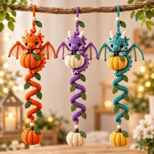 May include: Three hanging crochet ornaments featuring small dragons in orange, purple, and teal. Each dragon holds a small pumpkin and sits atop a long, spiralling vine with green leaves, ending in a second pumpkin at the bottom of each piece.