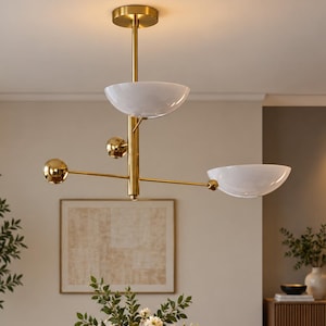 May include: A gold-toned metal chandelier featuring a central vertical rod, two white glass bowl-shaped shades, and two decorative gold spheres extending from the center on thin horizontal arms, suspended from a circular gold ceiling canopy.