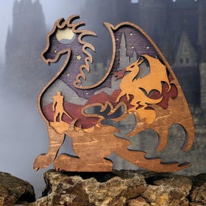 Puede incluir: Una escultura de dragón de madera con detalles intrincados, que presenta un dragón más pequeño en su interior. La escultura está pintada en tonos marrones, rojos y azules, con un fondo de cielo nocturno estrellado.