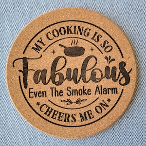 Puede incluir: Un posavasos redondo de corcho con un diseño negro que dice "Mi cocina es tan fabulosa que incluso la alarma de humo me anima".