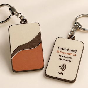 Pode incluir: Dois porta-chaves retangulares com argolas de metal prateado. Um apresenta um design ondulado em creme, castanho escuro e terracota. O outro é creme com o texto Found me? Scan NFC To contact my owner e um ícone NFC impressos.