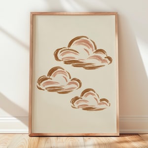 Peut inclure: Une affiche encadrée rectangulaire représentant trois nuages peints à la main dans des tons de brun, de beige et de rose pâle sur un fond crème uni. Le cadre en bois présente une finition naturelle claire entourant l'impression.