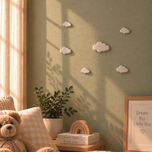 Puede incluir: Un conjunto de seis decoraciones de pared blancas con forma de nube montadas sobre una pared verde salvia. Las nubes varían en tamaño y están dispuestas en un patrón disperso. La decoración de pared presenta bordes lisos y redondeados y un acabado mate.