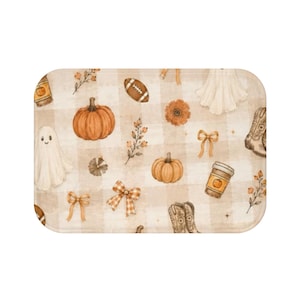Op de afbeelding: Een rechthoekige badmat met een beige en wit ruitpatroon, versierd met oranje pompoenen, witte spoken, bruine voetballen, beige cowboylaarzen, koffiebekers, strikken en bloemtakjes in een herhalend herfstontwerp.