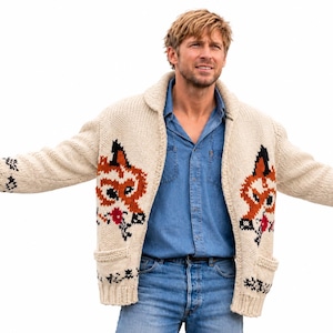 May include: A cream-colored chunky knit cardigan featuring a shawl collar and two front pockets. The garment displays a repeating intarsia pattern of orange and black foxes with small red accents on the front panels and along the sleeves.