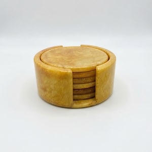 May include: A set of circular, golden-yellow stone coasters stacked neatly inside a matching cylindrical holder. The stone features a natural, mottled texture with varying shades of amber and honey, showcasing a smooth, polished finish throughout.