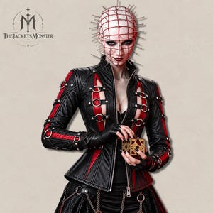 May include: A black and red leather jacket featuring silver metal rings, straps, and a front zipper closure. The garment includes vertical red panels, long sleeves with buckled straps, and a high collar. A gold-toned puzzle box is held in front.