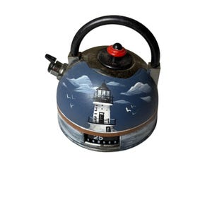Può includere: Un timer da cucina rotondo a forma di teiera in miniatura con manico nero e pomello rosso. Il corpo blu presenta un faro bianco dipinto a mano, nuvole e uccelli. Un quadrante meccanico alla base mostra il numero 25 in caratteri bianchi.