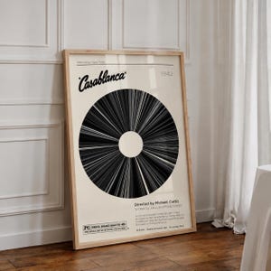 Könnte beinhalten: Ein gerahmtes Filmplakat für Casablanca, 1942, mit einer großen schwarz-weißen kreisförmigen Grafik, die an eine Schallplatte erinnert. Der cremefarbene Hintergrund enthält den Filmtitel, Regisseur Michael Curtiz und eine Inhaltsangabe.