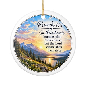 May include: A round white ceramic ornament featuring a gold hanging string. The center displays a landscape of mountains, a lake, and a sunrise with the text: Proverbs 16:9, In their hearts humans plan their course, but the Lord establishes their steps.