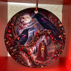 May include: A circular ornament featuring a detailed illustration of two black ravens perched on branches amidst autumn foliage. One raven holds a golden key in its beak. The scene includes a full moon, a stone gate, and a glowing lantern.