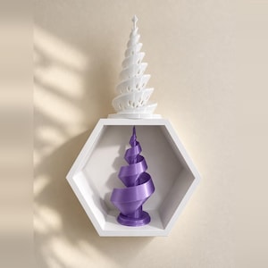 Puede incluir: Una escultura de árbol en espiral blanca se asienta sobre un estante de pared hexagonal blanco, que contiene una escultura de árbol en espiral morada. Ambas esculturas presentan un diseño cónico y retorcido con una punta superior.