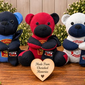 May include: Three plush teddy bears crafted from fabric, each featuring a dark nose, black eyes, and a firefighter-themed emblem on the chest. The bears are colored blue, red, and light gray, and each wears a dark scarf with a small fire truck graphic.