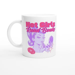 Op de afbeelding: Een witte keramische mok met een grafische illustratie van een persoon die lippenstift aanbrengt met een compactspiegel. De tekst "Hot Girls Read Books" staat in roze en paars boven de illustratie, vergezeld door een rode lippenafdruk.