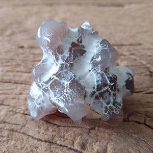 May include: A polished, irregular mineral specimen featuring translucent, light purple and grey tones contrasted by opaque, white, web-like veining across its surface. The stone has a smooth, glossy texture with rounded, bulbous protrusions and deep crevices.