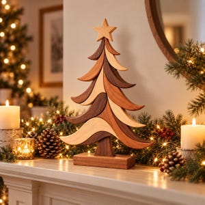 May include: A decorative tabletop Christmas tree sculpture crafted from layered, multi-toned natural wood pieces. The tree features a smooth, curved design with a star topper and a rectangular base, showcasing light, medium, and dark wood grains.