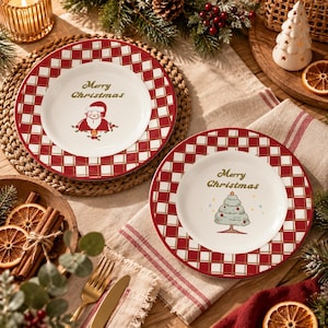 Peut inclure: Deux assiettes en céramique blanche avec une bordure à carreaux rouges et blancs. Une assiette présente une illustration du Père Noël et le texte Merry Christmas. L'autre affiche un sapin de Noël et le texte Merry Christmas.