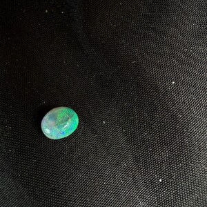 Peut inclure: Une pierre pr&eacute;cieuse opale de forme ovale lisse, pr&eacute;sentant une base translucide avec des &eacute;clats vibrants de lumi&egrave;re verte et bleue. La pierre affiche une surface polie et arrondie qui refl&egrave;te la lumi&egrave;re, r&eacute;v&eacute;lant un jeu de couleurs distinct.
