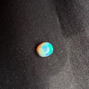 Peut inclure: Une pierre pr&eacute;cieuse opale de forme ovale et lisse pr&eacute;sentant un jeu de couleurs vibrant avec des &eacute;clats iridescents orange, verts et bleus sur sa surface polie. La pierre poss&egrave;de une qualit&eacute; translucide et une taille cabochon arrondie.