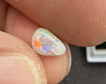 Peut inclure: Une petite pierre précieuse opale en forme de goutte d'eau, dotée d'une base blanche translucide avec des éclats vibrants de rouge, orange, jaune, vert et bleu sur toute sa surface polie, lisse et légèrement bombée.