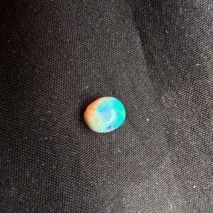 Peut inclure: Une pierre pr&eacute;cieuse opale de forme ovale et lisse, pr&eacute;sentant un jeu de couleurs vibrant avec des &eacute;clats iridescents de tons orange vif, vert n&eacute;on et bleu profond sur sa surface polie et translucide, offrant un aspect naturel multicolore.