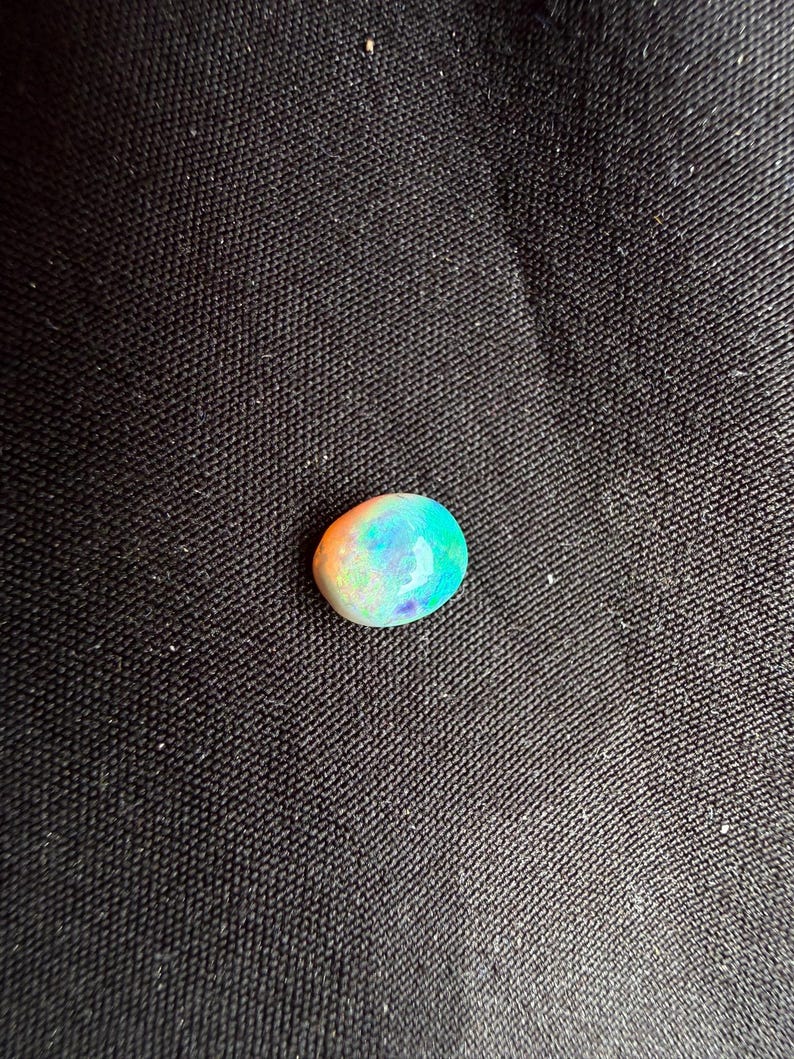 Peut inclure: Une pierre pr&eacute;cieuse opale de forme ovale et lisse, pr&eacute;sentant un jeu de couleurs vibrant avec des &eacute;clats iridescents de tons orange vif, vert n&eacute;on et bleu profond sur sa surface polie et translucide, offrant un aspect naturel multicolore.