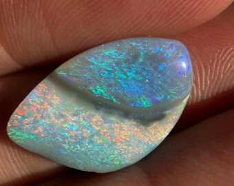 May include: A polished, teardrop-shaped opal gemstone featuring a vibrant play-of-color with flashes of bright green, electric blue, and fiery orange against a light, semi-translucent base. The stone has a smooth, undulating surface texture.
