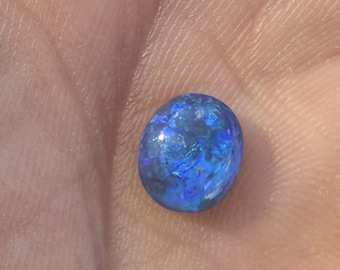 Peut inclure: Une petite pierre précieuse de forme ovale avec une surface lisse et polie. La pierre présente une couleur de base bleu profond et vibrante avec des éclats irisés de bleu plus clair et des touches de vert dans sa structure cristalline.