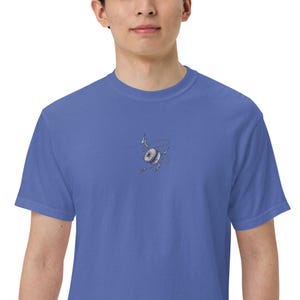May include: A blue short-sleeved t-shirt featuring a small, centered embroidered graphic of a grey yo-yo surrounded by a thin, winding string and two small lightning bolt symbols. The design is positioned on the chest area of the garment.