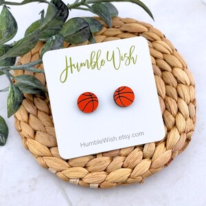 Peut inclure: Boucles d'oreilles &agrave; clous en forme de ballons de basket-ball orange avec des lignes noires. Elles sont pr&eacute;sent&eacute;es sur une carte blanche avec le texte "Humble Wish" et "HumbleWish.etsy.com". Le fond est un tapis tress&eacute;.