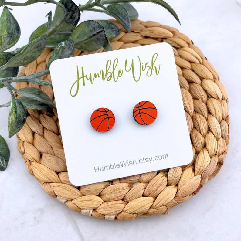 Peut inclure: Boucles d'oreilles &agrave; clous en forme de ballons de basket-ball orange avec des lignes noires. Elles sont pr&eacute;sent&eacute;es sur une carte blanche avec le texte "Humble Wish" et "HumbleWish.etsy.com". Le fond est un tapis tress&eacute;.