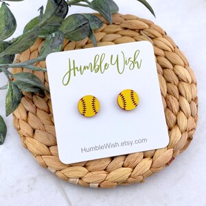 Peut inclure: Boucles d'oreilles clous en forme de balle de softball jaune avec des coutures rouges. Elles sont pr&eacute;sent&eacute;es sur une carte blanche avec le texte "Humble Wish" et "HumbleWish.etsy.com". Pos&eacute;es sur un dessous de plat tress&eacute;.