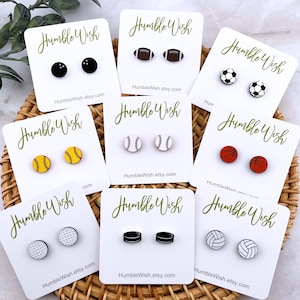 Peut inclure: Une collection de boucles d'oreilles &agrave; clous sur le th&egrave;me du sport, chacune repr&eacute;sentant un sport diff&eacute;rent : bowling, football am&eacute;ricain, football, baseball, basket-ball, golf, palets de hockey et volley-ball. Chaque paire est pr&eacute;sent&eacute;e sur une carte blanche.