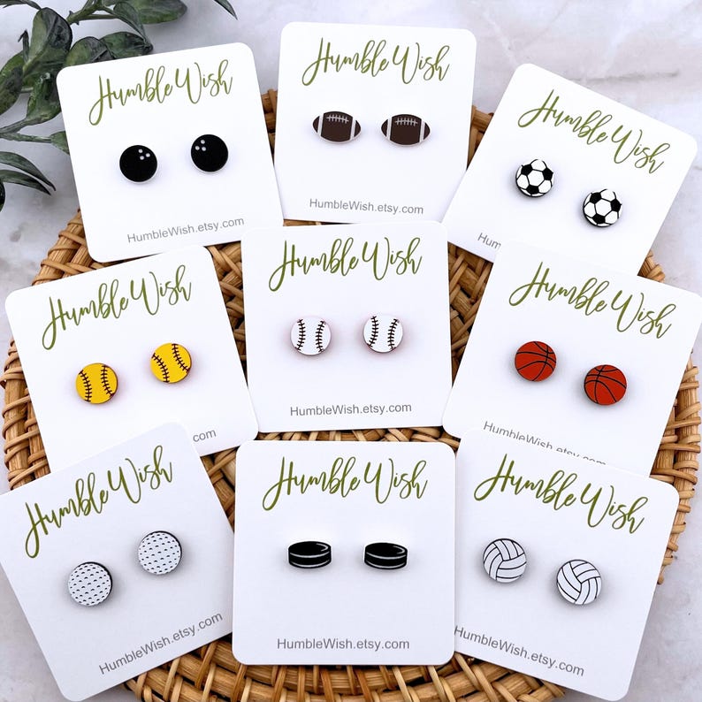 Peut inclure: Une collection de boucles d'oreilles &agrave; clous sur le th&egrave;me du sport, chacune repr&eacute;sentant un sport diff&eacute;rent : bowling, football am&eacute;ricain, football, baseball, basket-ball, golf, palets de hockey et volley-ball. Chaque paire est pr&eacute;sent&eacute;e sur une carte blanche.