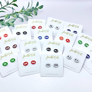 May include: A set of 12 pairs of oval-shaped earrings with different running distances and race types printed on them. The earrings are white with black text, red with white text, green with white text, blue with white text, and black with white text. The earrings are displayed on white cards with the text "Humble Wish" printed on them.