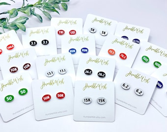 May include: A set of 12 pairs of oval-shaped earrings with different running distances and race types printed on them. The earrings are white with black text, red with white text, green with white text, blue with white text, and black with white text. The earrings are displayed on white cards with the text "Humble Wish" printed on them.