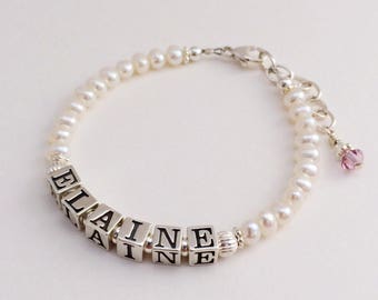 Puede incluir: Un brazalete de perlas blancas con un dije de plata que deletrea el nombre "ELAINE". El brazalete tiene un cierre de plata y un pequeño dije de cristal rosa.