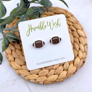 May include: A pair of brown and white football-shaped stud earrings on a white card with the text "Humble Wish" and "HumbleWish.etsy.com".