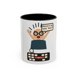 May include: A white ceramic mug with a black interior and rim, featuring a graphic of a frustrated character with glasses at a keyboard. A speech bubble contains the text 'there's no 'any' key?!' and the keyboard has a red key labelled 'any?'.