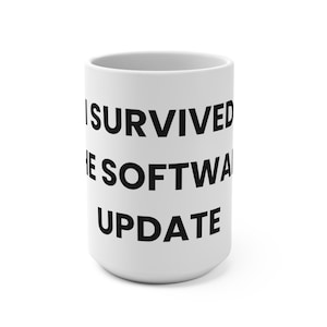 Könnte beinhalten: Ein weißer Keramikbecher mit dem in Schwarz aufgedruckten Text I SURVIVED THE SOFTWARE UPDATE in einer fetten, serifenlosen Schrift. Der Becher hat eine zylindrische Form mit einer glatten Oberfläche und einer weiten Öffnung an der Oberseite.